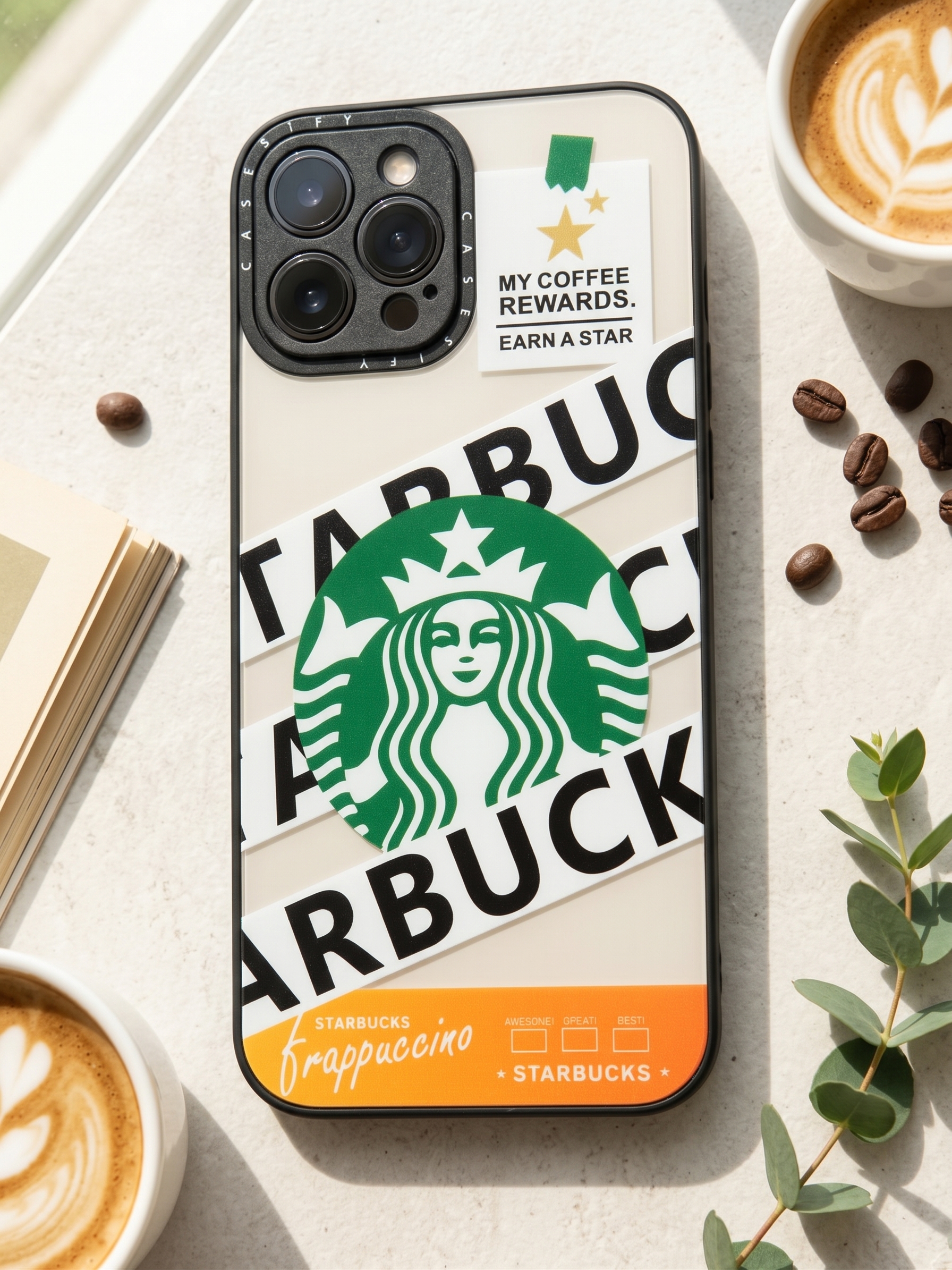 ‏قاب گوشی آیفون 12 پرو مکس طرح گرافیکی قهوه استارباکس Starbucks با زمینه سفید و بامپر مشکی ضد ضربه در کنار فنجان قهوه لاته و دانه‌های قهوه